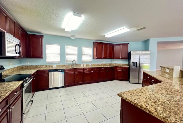 kitchen featuring light tile patterned flooring, sink, a textured ceiling, stainless steel appliances, and light stone countertops