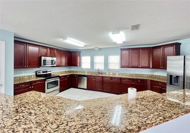 kitchen featuring light stone counters, light tile patterned floors, sink, a textured ceiling, and appliances with stainless steel finishes