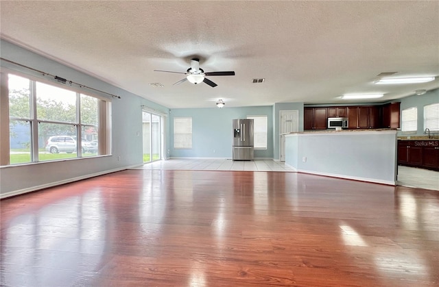 unfurnished living room with light hardwood / wood-style floors, ceiling fan, and a textured ceiling