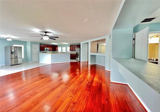 unfurnished living room featuring light hardwood / wood-style flooring, a textured ceiling, and ceiling fan