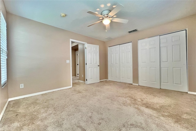 unfurnished bedroom with two closets, ceiling fan, and light colored carpet