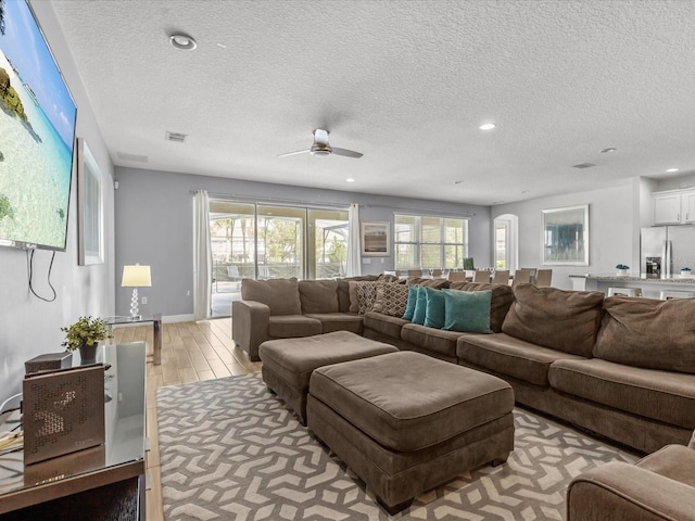 living room featuring light wood-type flooring, plenty of natural light, visible vents, and a textured ceiling