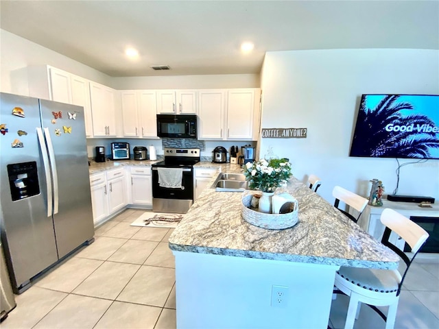 kitchen with a breakfast bar area, light tile patterned floors, light stone counters, white cabinetry, and stainless steel appliances