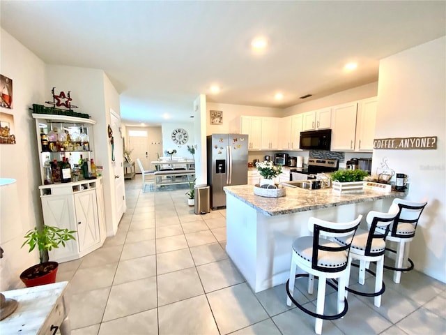 kitchen with white cabinets, light tile patterned floors, light stone counters, kitchen peninsula, and stainless steel appliances