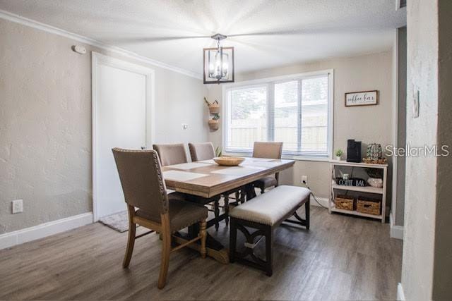 dining area featuring a textured ceiling, dark wood-type flooring, crown molding, and a notable chandelier