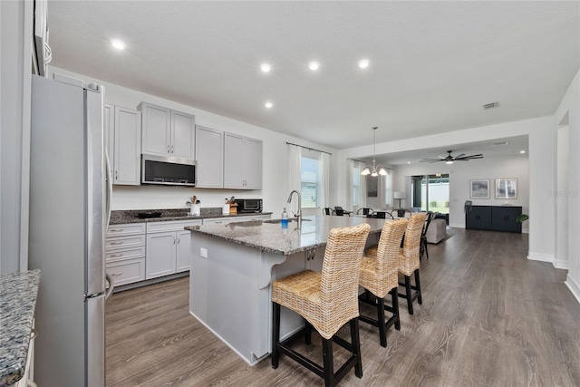 kitchen featuring a breakfast bar, stainless steel appliances, light stone countertops, hardwood / wood-style floors, and a center island with sink