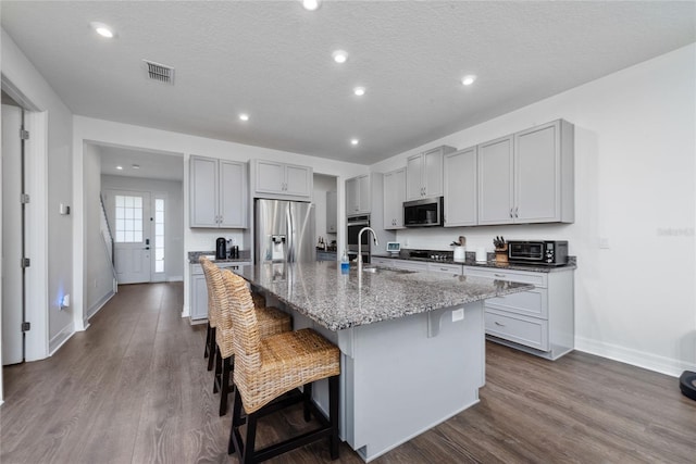 kitchen featuring appliances with stainless steel finishes, hardwood / wood-style floors, a breakfast bar, sink, and an island with sink