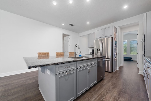 kitchen with a center island with sink, dark wood-type flooring, gray cabinets, appliances with stainless steel finishes, and sink