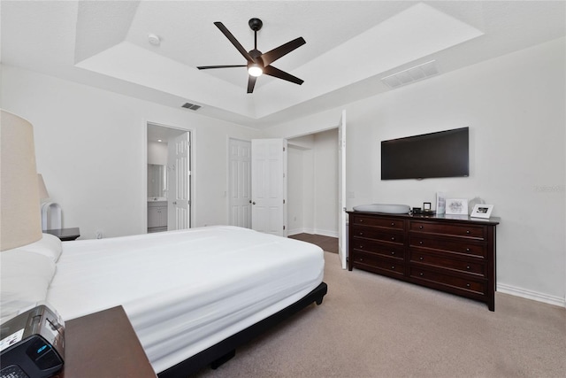 bedroom with ceiling fan, ensuite bathroom, a tray ceiling, and light colored carpet