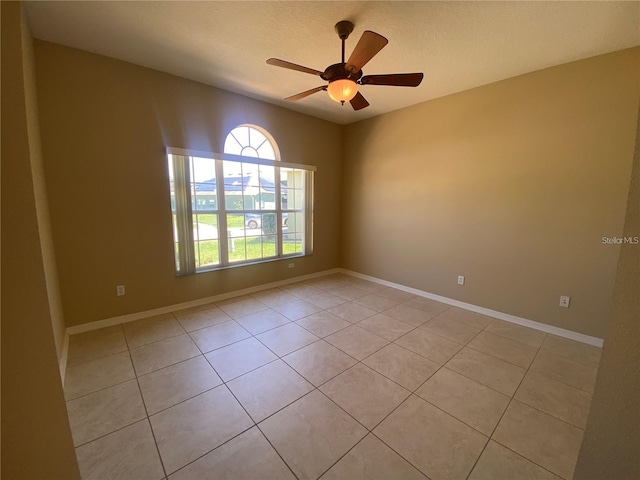 empty room featuring light tile patterned floors, a ceiling fan, and baseboards