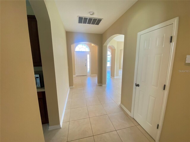 corridor with arched walkways, visible vents, baseboards, and light tile patterned flooring