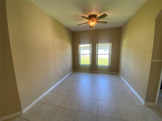 empty room featuring light tile patterned flooring, a ceiling fan, and baseboards