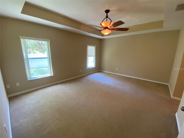 carpeted empty room with ceiling fan and a raised ceiling