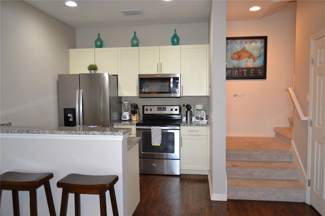 kitchen featuring dark wood-type flooring, appliances with stainless steel finishes, white cabinetry, light stone counters, and decorative backsplash