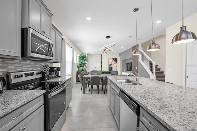 kitchen with decorative light fixtures, sink, backsplash, light stone counters, and stainless steel appliances