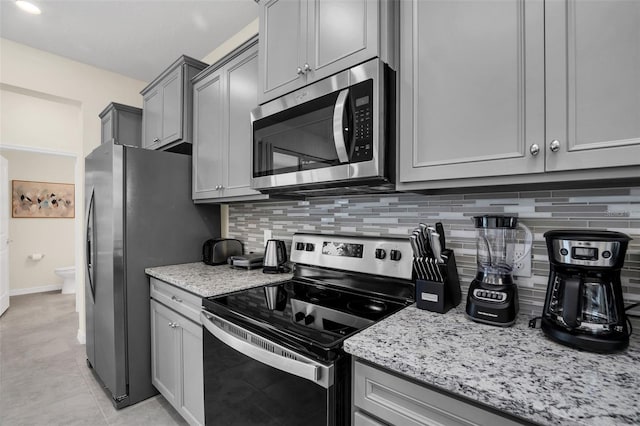 kitchen with light tile patterned floors, gray cabinetry, backsplash, stainless steel appliances, and light stone counters