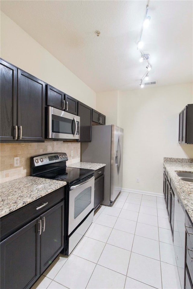 kitchen featuring decorative backsplash, light stone countertops, light tile patterned floors, and appliances with stainless steel finishes