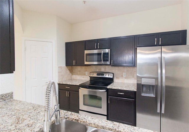 kitchen with decorative backsplash, stainless steel appliances, and light stone countertops