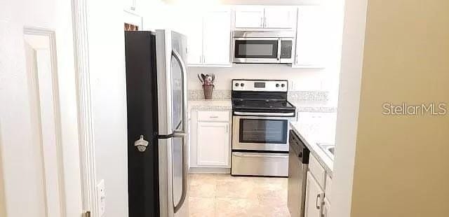 kitchen with stainless steel appliances, white cabinetry, and light tile floors