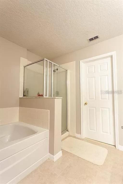 bathroom with tile floors, a textured ceiling, and separate shower and tub