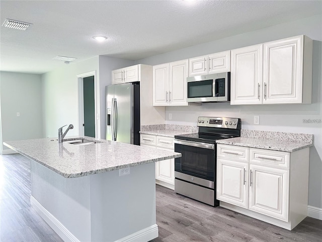 kitchen featuring white cabinetry, sink, a center island with sink, appliances with stainless steel finishes, and light hardwood / wood-style flooring