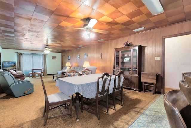 carpeted dining room with ceiling fan and wooden walls