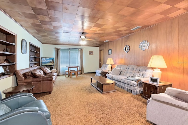 living area with visible vents, a ceiling fan, carpet floors, wood walls, and built in shelves