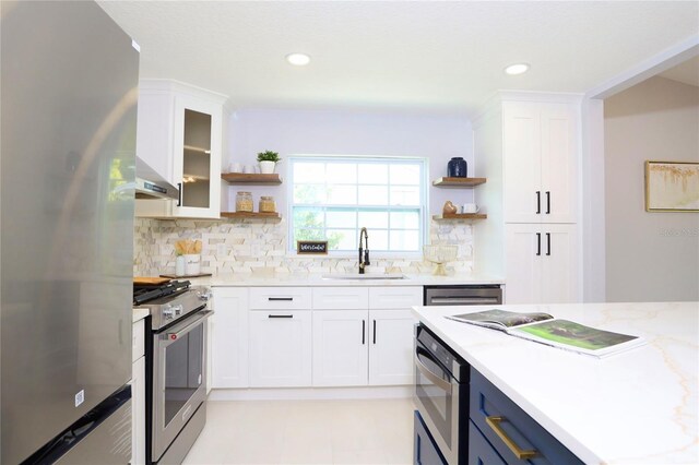 kitchen featuring appliances with stainless steel finishes, light stone countertops, range hood, white cabinets, and sink