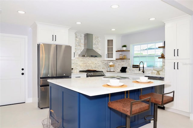 kitchen with a center island, a kitchen bar, stainless steel appliances, white cabinets, and wall chimney exhaust hood