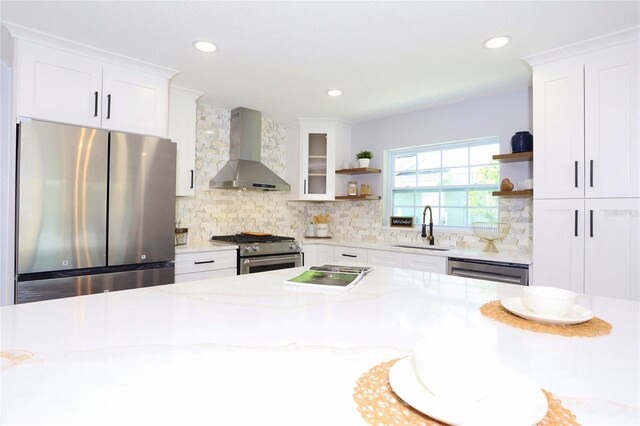 kitchen featuring white cabinetry, appliances with stainless steel finishes, light stone countertops, wall chimney exhaust hood, and sink