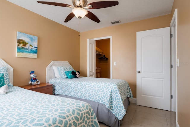 bedroom featuring a walk in closet, a textured ceiling, a closet, ceiling fan, and light tile floors