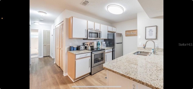 kitchen with light hardwood / wood-style flooring, white cabinets, stainless steel appliances, light stone countertops, and sink