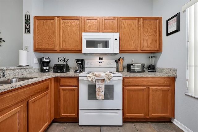 kitchen with light tile patterned flooring, light stone countertops, sink, and white appliances