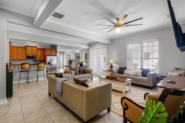 living room with light tile patterned flooring, ceiling fan, ornamental molding, and a textured ceiling