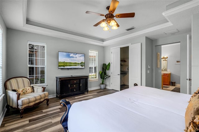 bedroom with ensuite bath, dark hardwood / wood-style floors, ceiling fan, and a tray ceiling