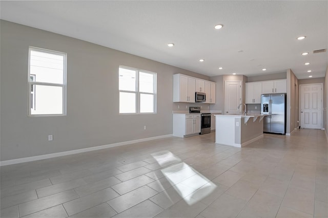 kitchen featuring light tile patterned flooring, a kitchen island with sink, a healthy amount of sunlight, white cabinetry, and stainless steel appliances