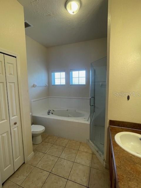 bathroom featuring a relaxing tiled tub, a textured ceiling, tile patterned floors, toilet, and vanity