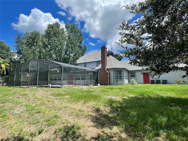 rear view of property with glass enclosure and a lawn