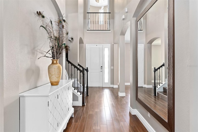 entryway featuring stairway, arched walkways, a high ceiling, baseboards, and dark wood-style flooring