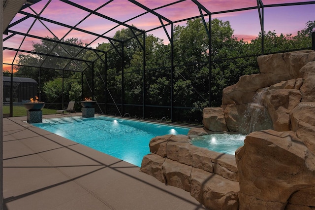 pool at dusk with pool water feature, glass enclosure, a patio area, and a hot tub