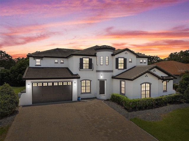 mediterranean / spanish house featuring a garage, stucco siding, driveway, and a tile roof