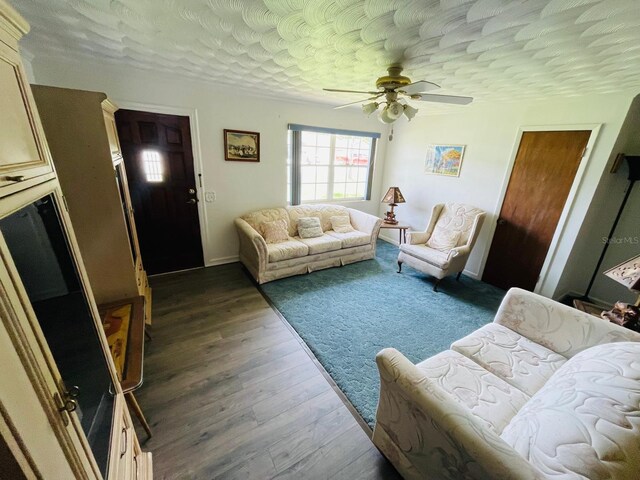 living room featuring ceiling fan, a textured ceiling, and dark wood-type flooring