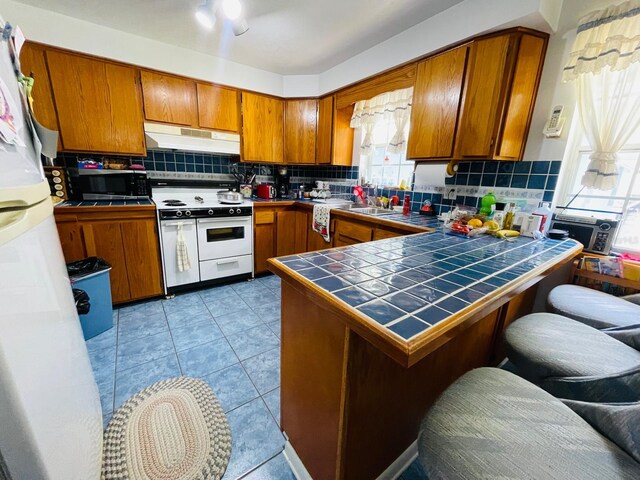 kitchen featuring tile counters, tasteful backsplash, kitchen peninsula, white appliances, and light tile patterned floors