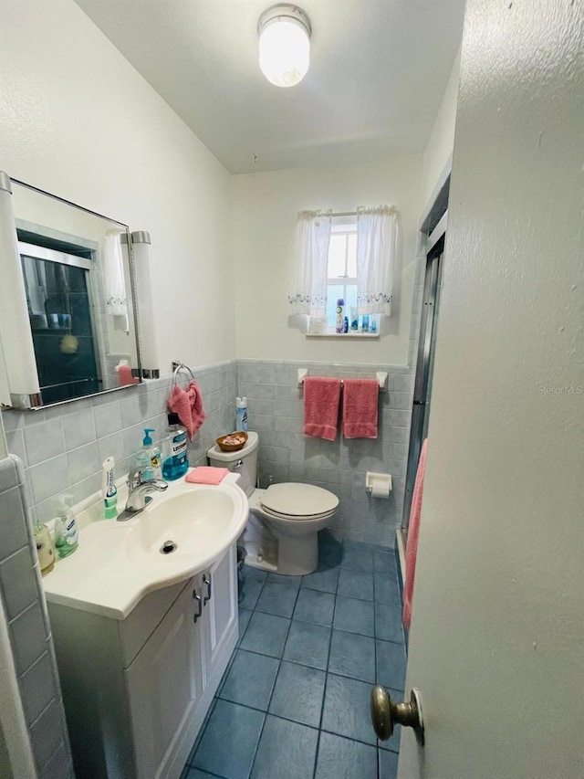 bathroom with tile walls, tile patterned flooring, a shower with shower door, vanity, and toilet