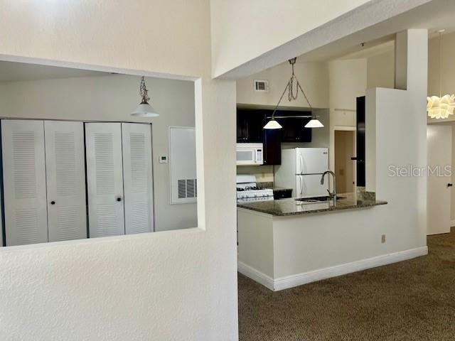 kitchen featuring dark carpet, white appliances, sink, and hanging light fixtures