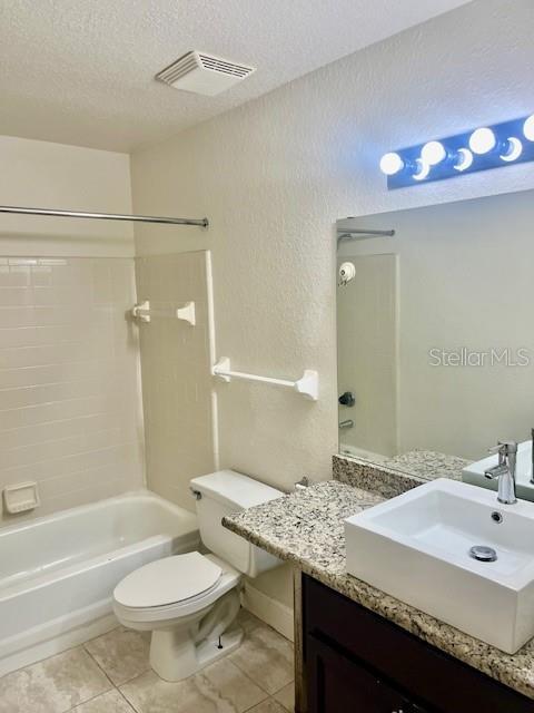 full bathroom featuring tile patterned flooring, a textured ceiling, shower / washtub combination, toilet, and vanity