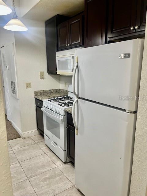 kitchen with light stone counters, white appliances, dark brown cabinets, and light tile patterned flooring