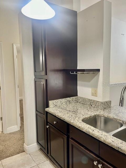 kitchen with light stone countertops, sink, light tile patterned flooring, and dark brown cabinetry