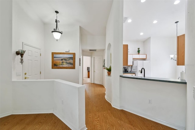 interior space with kitchen peninsula, light hardwood / wood-style floors, white fridge with ice dispenser, and hanging light fixtures