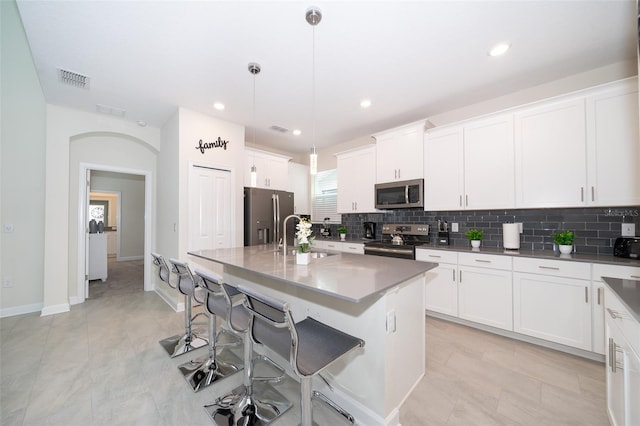 kitchen featuring light tile patterned floors, a kitchen island with sink, stainless steel appliances, pendant lighting, and sink